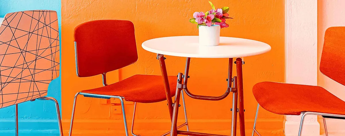 Rode eetkamerstoelen en een wit tafeltje voor een oranje muur